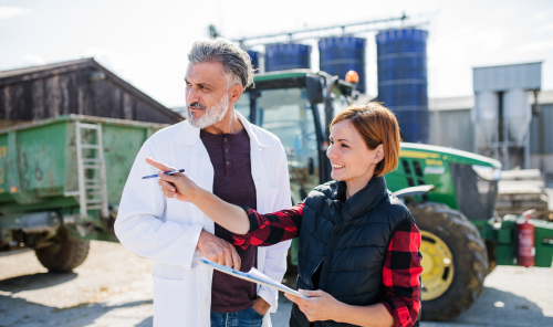 man and woman holding a clipboard infront of a tractor